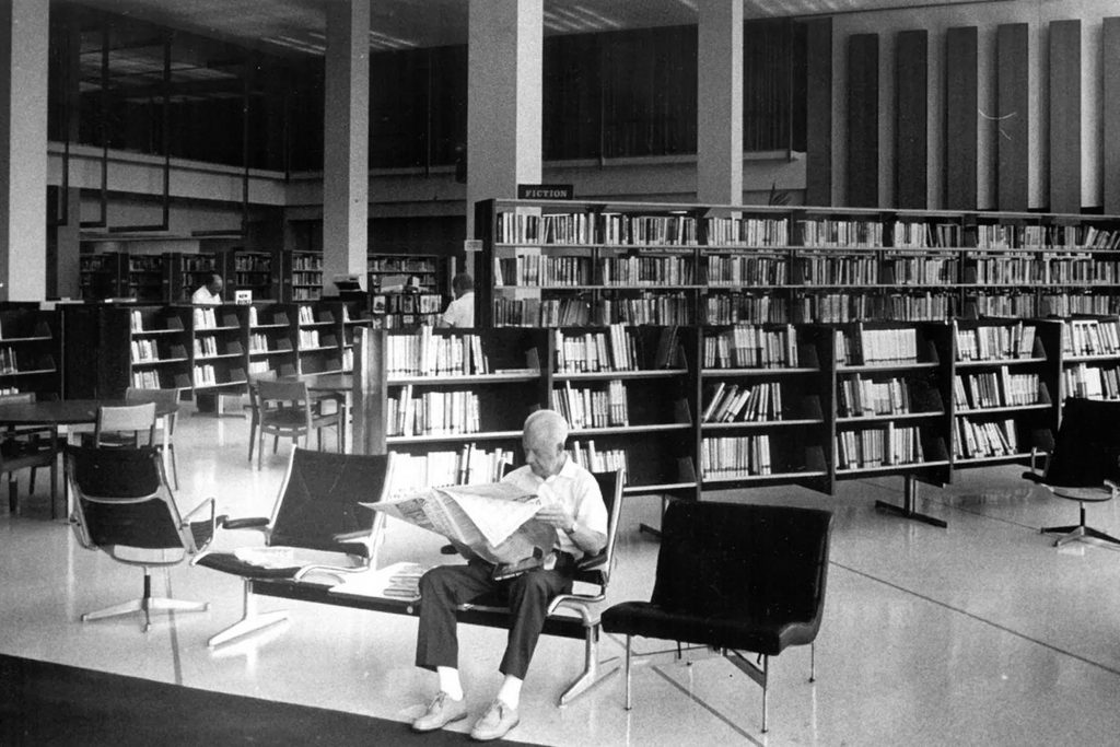 older black and white interior photo with a man sitting and reading a paper in the library | Photo/Don Burk, The Florida Times-Union